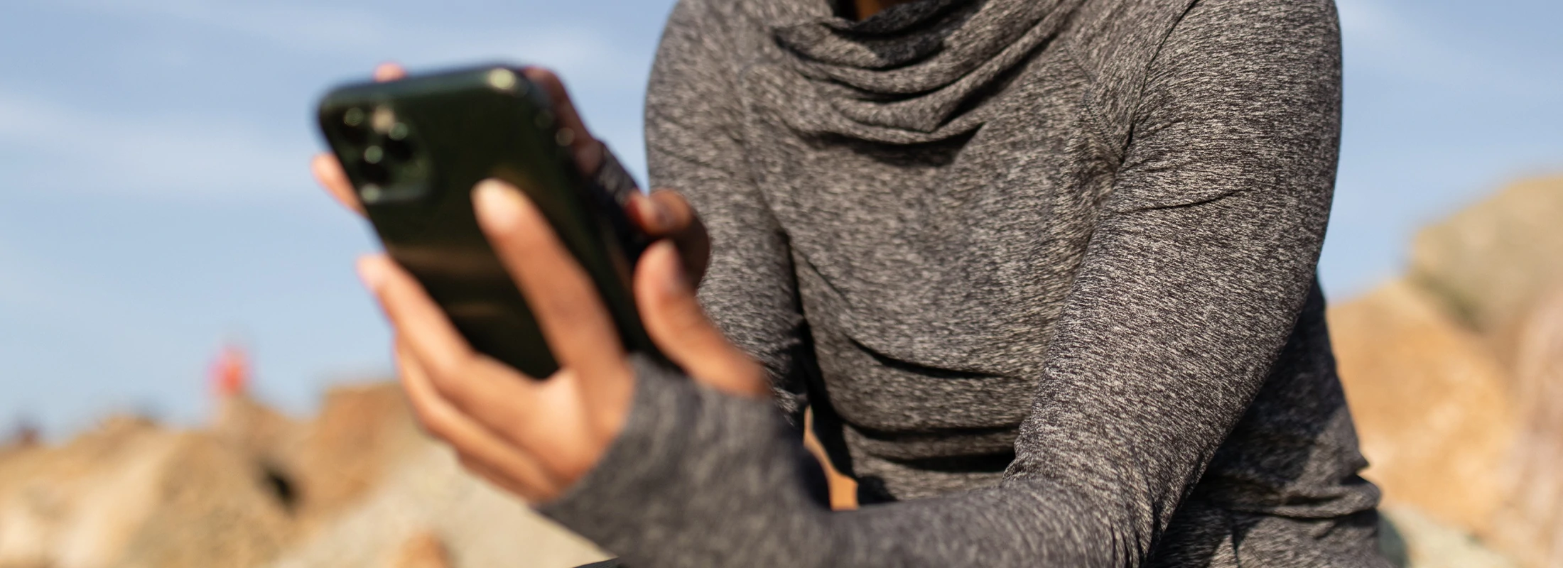 A person using their phone in a grey hipster sweatshirt with their thumb in a hole in the sleeve.